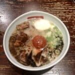 A bowl of ramen with custardy ramen eggs floating in the broth with tender chashu pork and a large mound of spicy tare topping