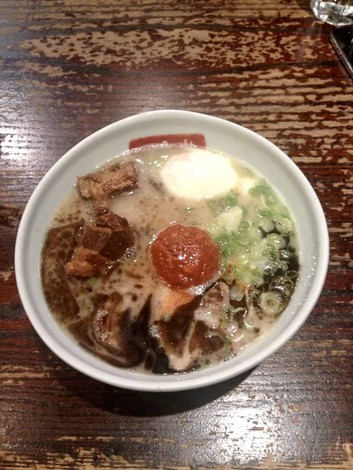 A bowl of ramen with custardy ramen eggs floating in the broth with tender chashu pork and a large mound of spicy tare topping
