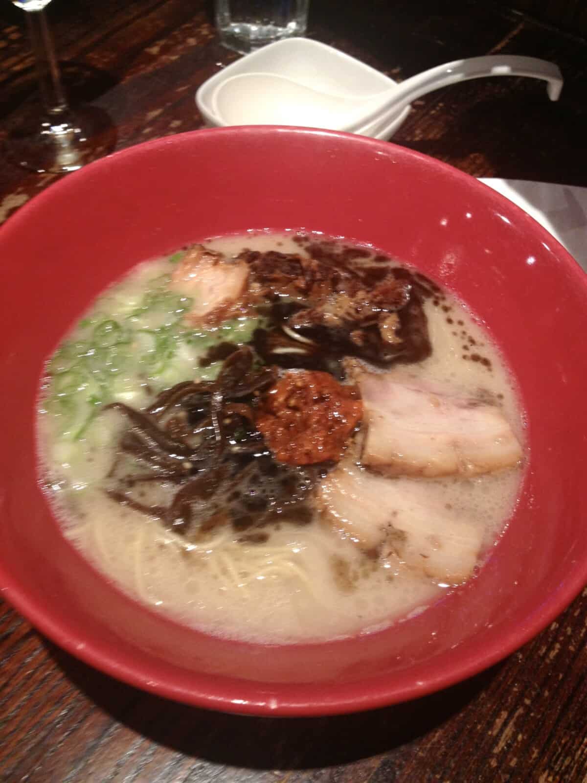 a red bowl of ramen in a milky tonkotsu broth, seaweed, chashu pork, scallions and spicy sauce in the middle