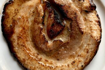 a piece of round beautifully golden brown quick-torched chashu pork on a plate