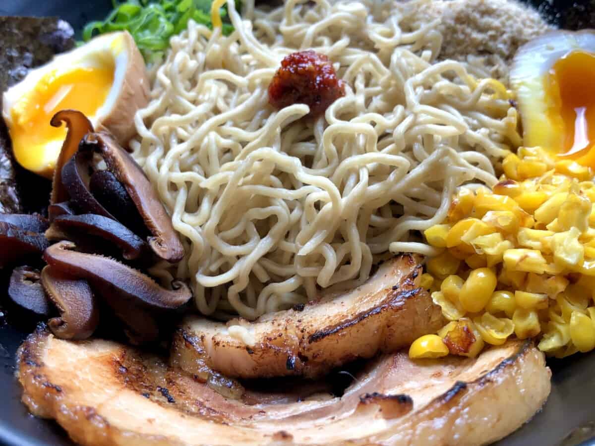 ramen toppings nested in a bowl around a pile of bouncy homemade ramen noodles