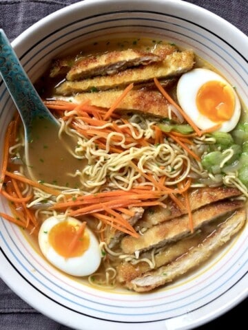 Bowl of homemade chicken noodle soup with ramen noodles, chicken katsu and ramen eggs plus sliced celery, julienned carrots, and toasted sesame seed for extra crunch.