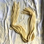 Perfect homemade egg noodles for chicken noodle soup resting on a flour-dusted tea towel, freshly cut and ready to cook from scratch.