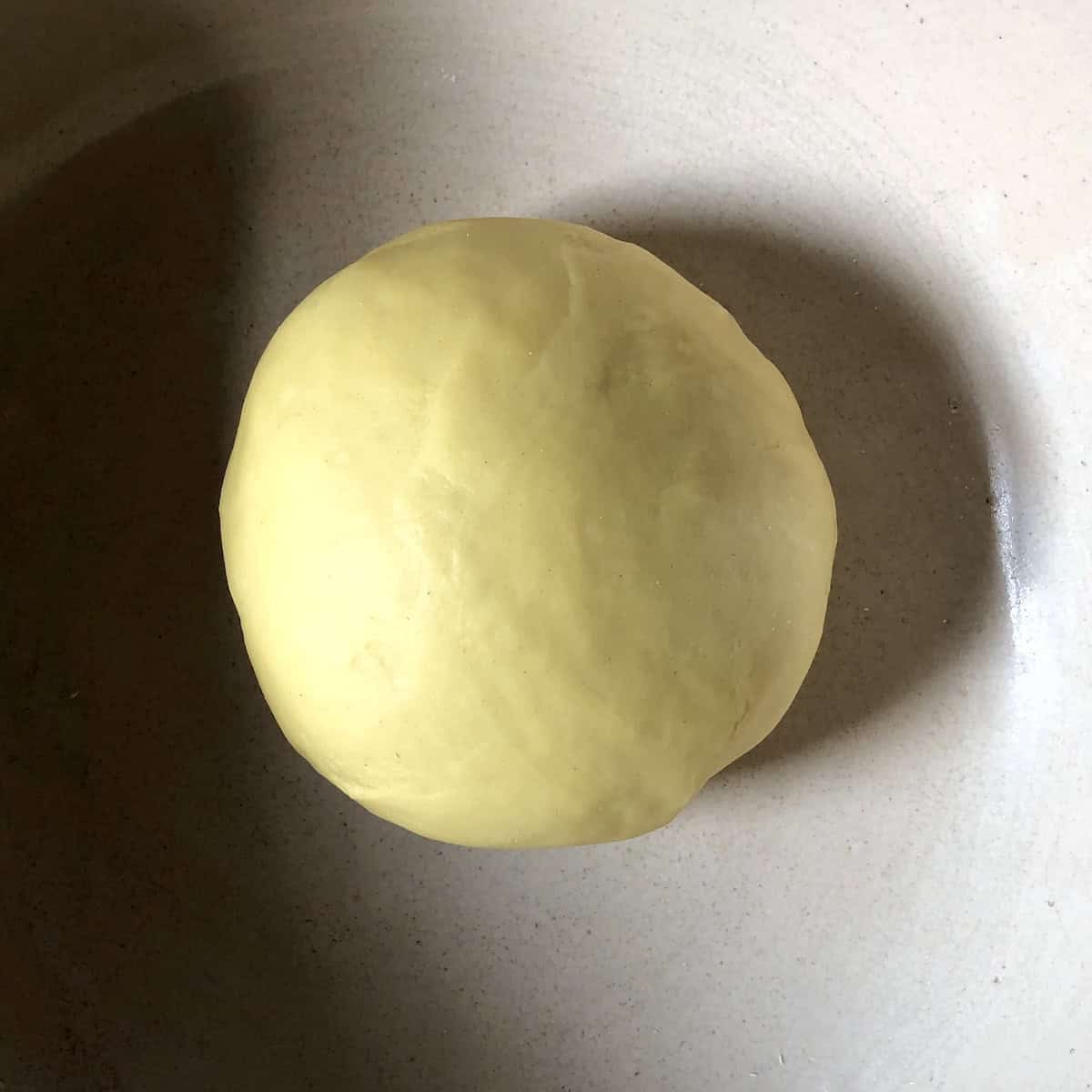 Rested egg noodle dough ball after 10 minutes showing deeper yellow color and smooth texture showing stage 3 of american style classic egg noodle dough.