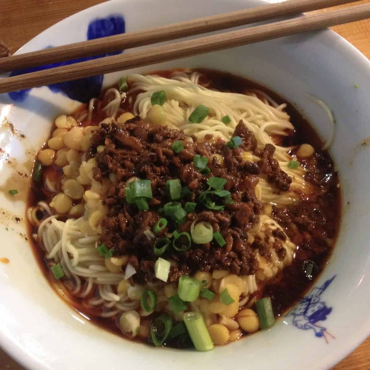 Famous Chengdu restaurant dan dan mian with chickpeas scallions crispy pork and very saucy traditional Sichuan noodles authentic dan dan noodles recipe.