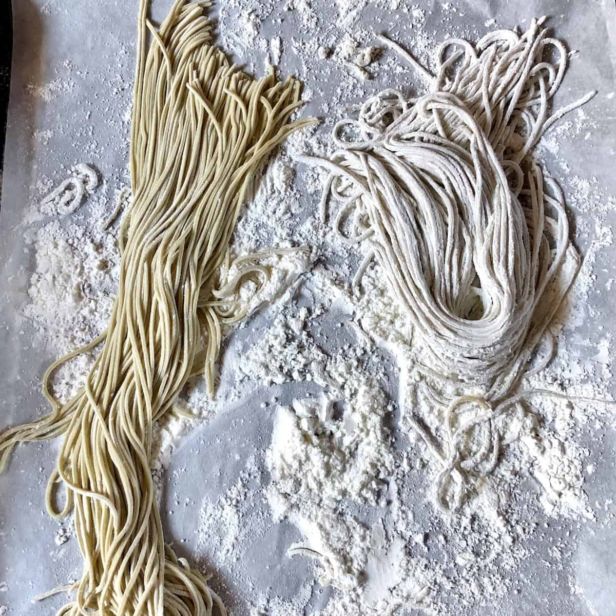 Side by side portioned finished ramen noodles on cornstarch dusted sheet tray showing proper storage technique with one portion covered in cornstarch and other freshly cut homemade ramen noodle.