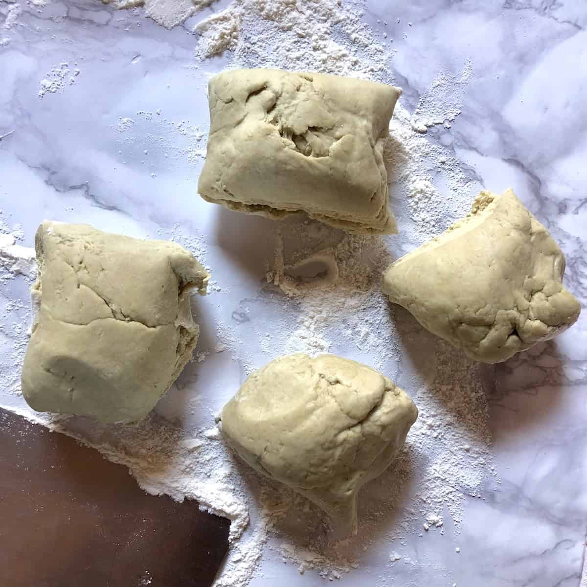 Four cut portions of rested ramen dough pieces ready for pasta machine rolling homemade ramen noodles recipe alkaline dough divided after overnight rest how to make ramen preparation step portioned dough for easier handling.
