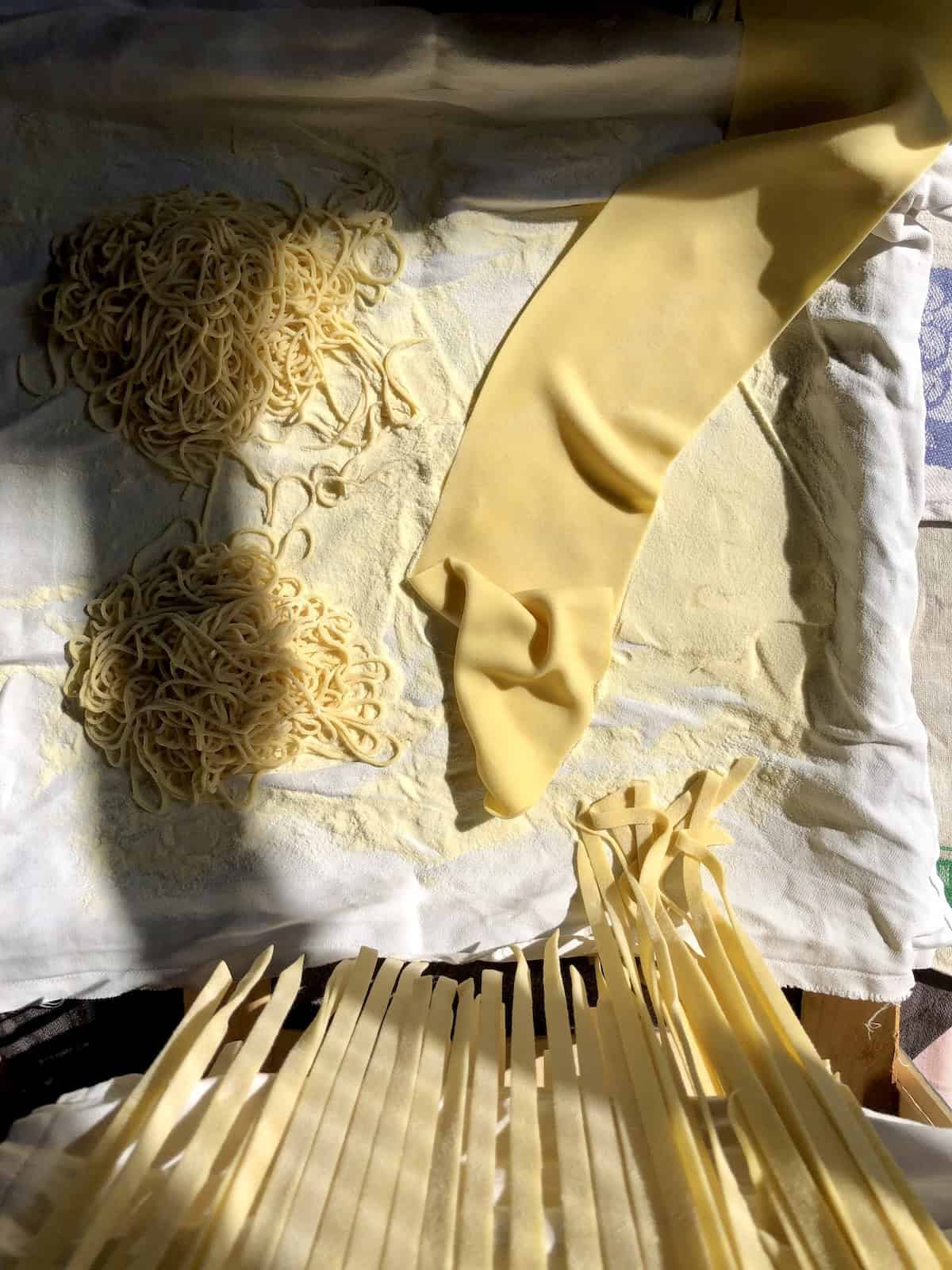 Homemade egg noodles displayed three ways: fettuccine-style chicken soup noodles coming out of a pasta machine, spaghetti egg noodle nests, and an uncut sheet of fresh egg pasta dough ready to be cut.