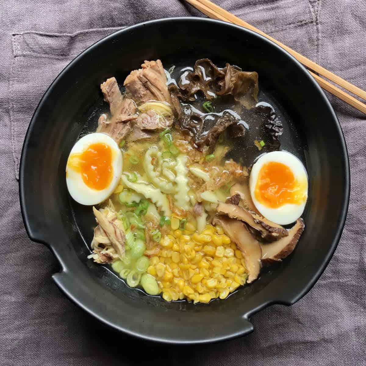 Homemade piping hot chicken ramen broth with homemade spinach udon noodles roasted chicken roasted pork ramen eggs wood ear mushrooms shiitake mushrooms scallions and corn showing complete ramen bowl recipe how to make chicken ramen homemade udon noodles.