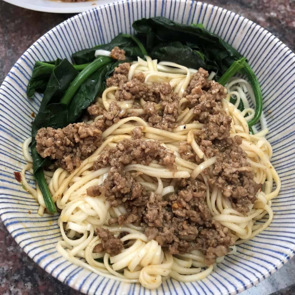 Authentic homemade Sichuan dan dan mian with homemade ramen noodles topped with bok choy and chives not mixed together yet showing traditional dan dan noodles recipe how to make dan dan mian Chinese noodles alkaline ramen noodles authentic preparation.
