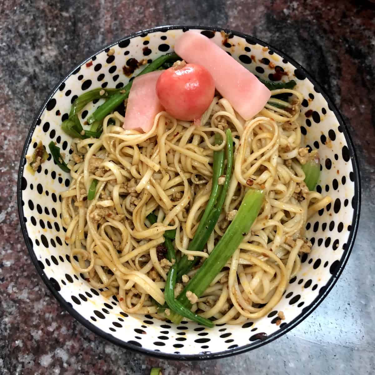 Homemade dan dan mian mixed together with chives bok choy and homemade Sichuan pao cai (Sichuan pickles) using homemade ramen noodles showing traditional Chinese dan dan noodles recipe.