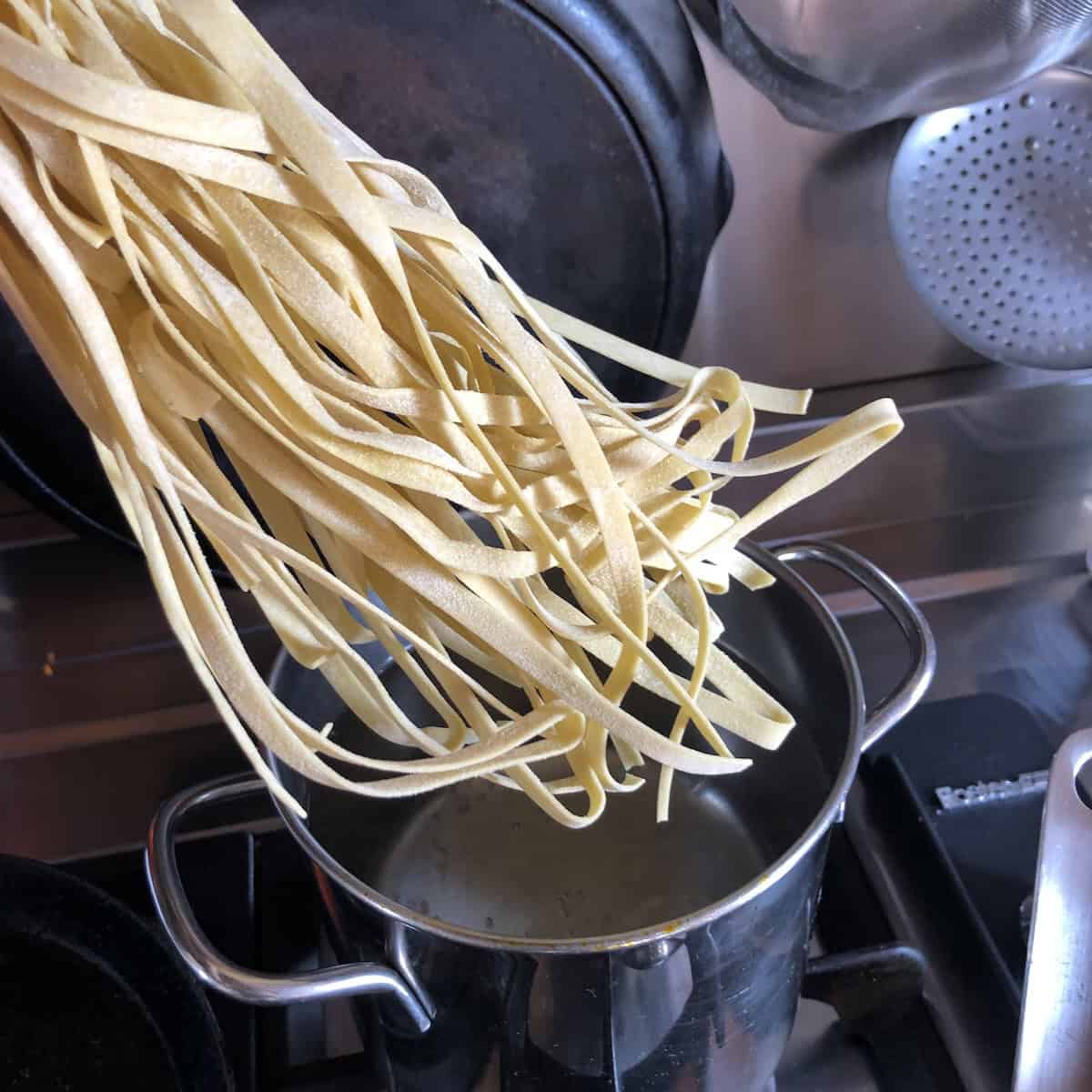 Classic homemade egg noodles fettuccine style added to boiling salted water, showing how to cook egg noodles.
