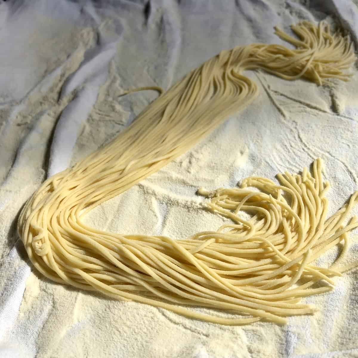 Homemade egg noodles for chicken soup cut with a chitarra pasta cutter, creating square spaghetti-style fresh noodles with a rustic shape.
