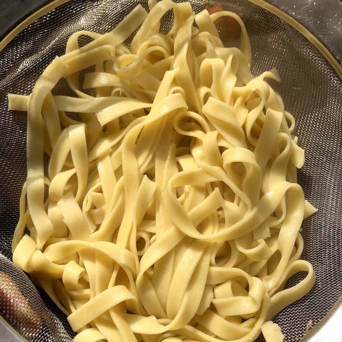 Homemade egg noodles freshly cooked in strainer ready to serve, fresh egg noodle recipe.