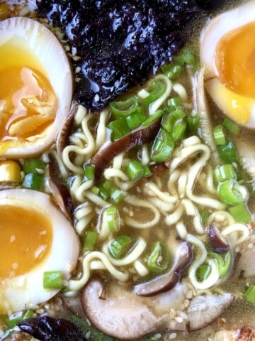 Bowl of homemade Japanese tonkotsu ramen with three halves of jammy perfectly cooked ramen eggs showing soft yolks and shoyu tare seasoning with traditional ramen toppings authentic tonkotsu ramen recipe.