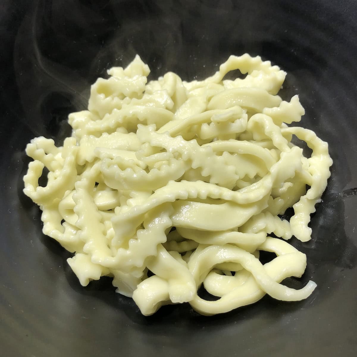 Bowl of pale green homemade spinach udon noodles just cooked and steaming hot showing thick green udon noodles fresh from boiling water homemade udon recipe.