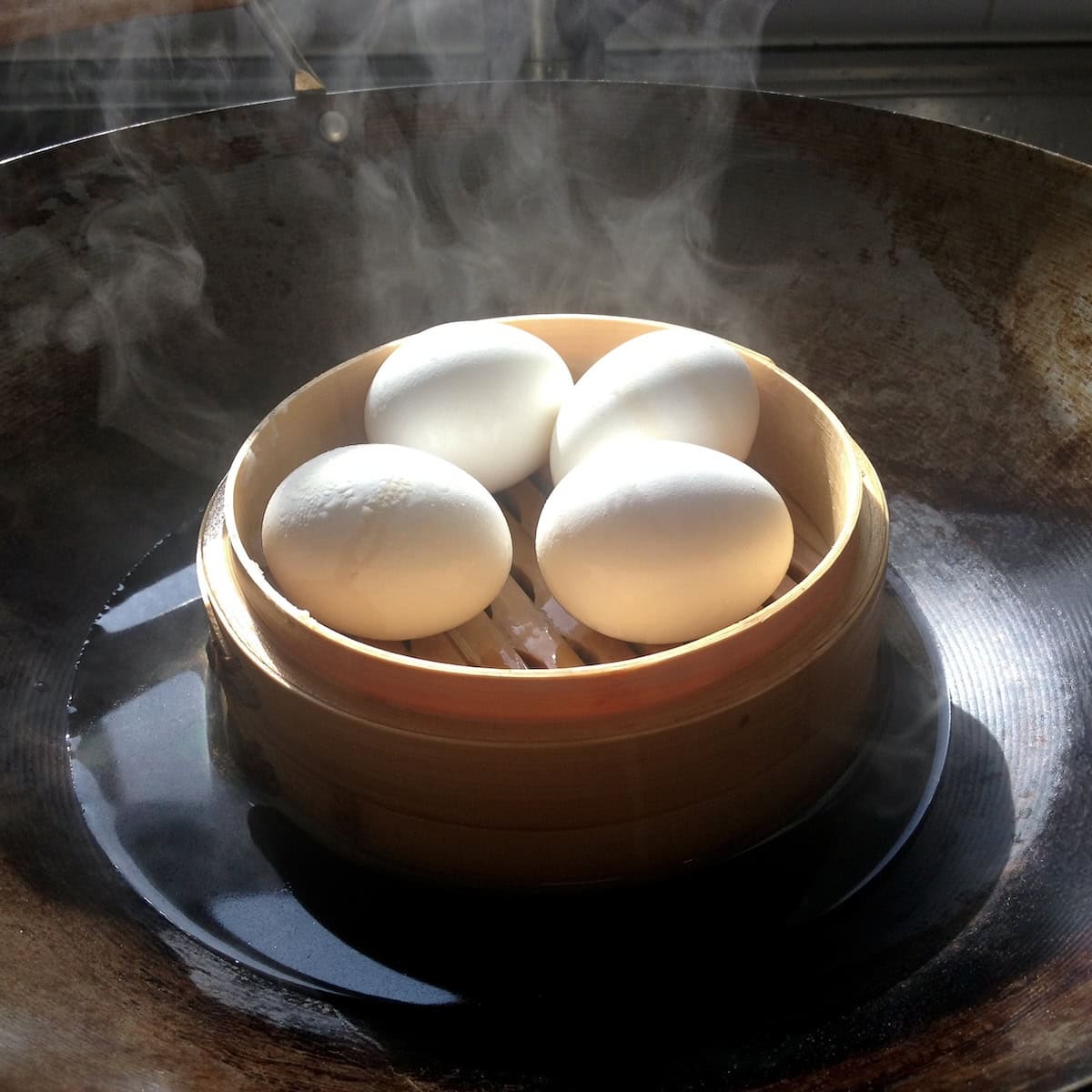 How to make ramen eggs in bamboo steamer showing 4 perfect soft boiled whole steamed eggs in wok with water (the  ajitsuke tamago cooking method for ramen egg recipe).
