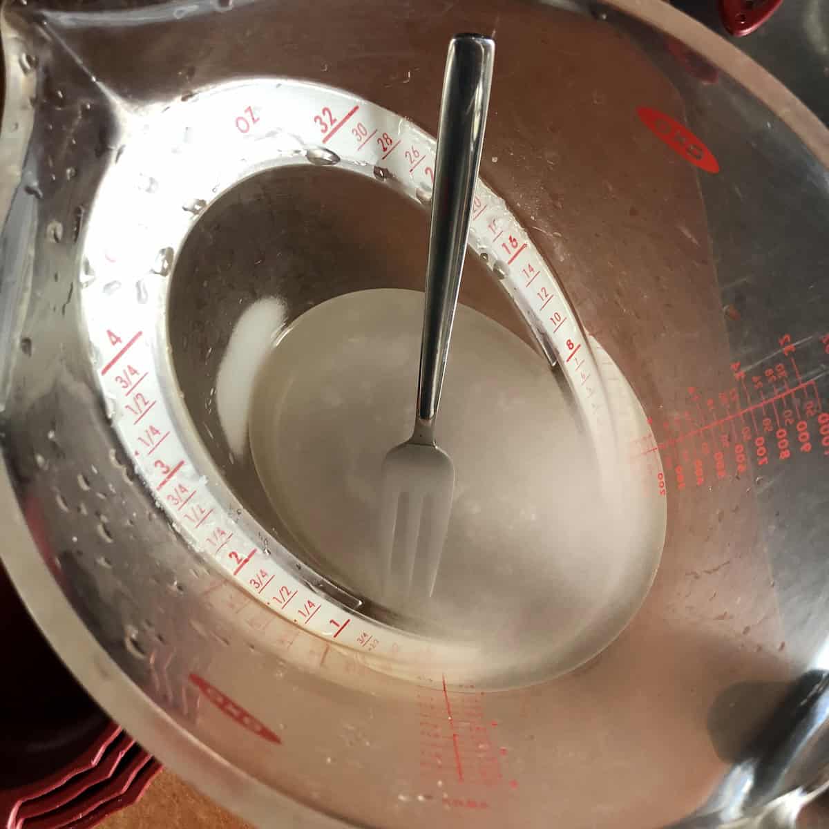 Alkaline water for homemade ramen noodles made by mixing baked baking soda and salt with water in measuring cup showing how to make ramen ingredients preparation step for authentic ramen recipe from scratch.