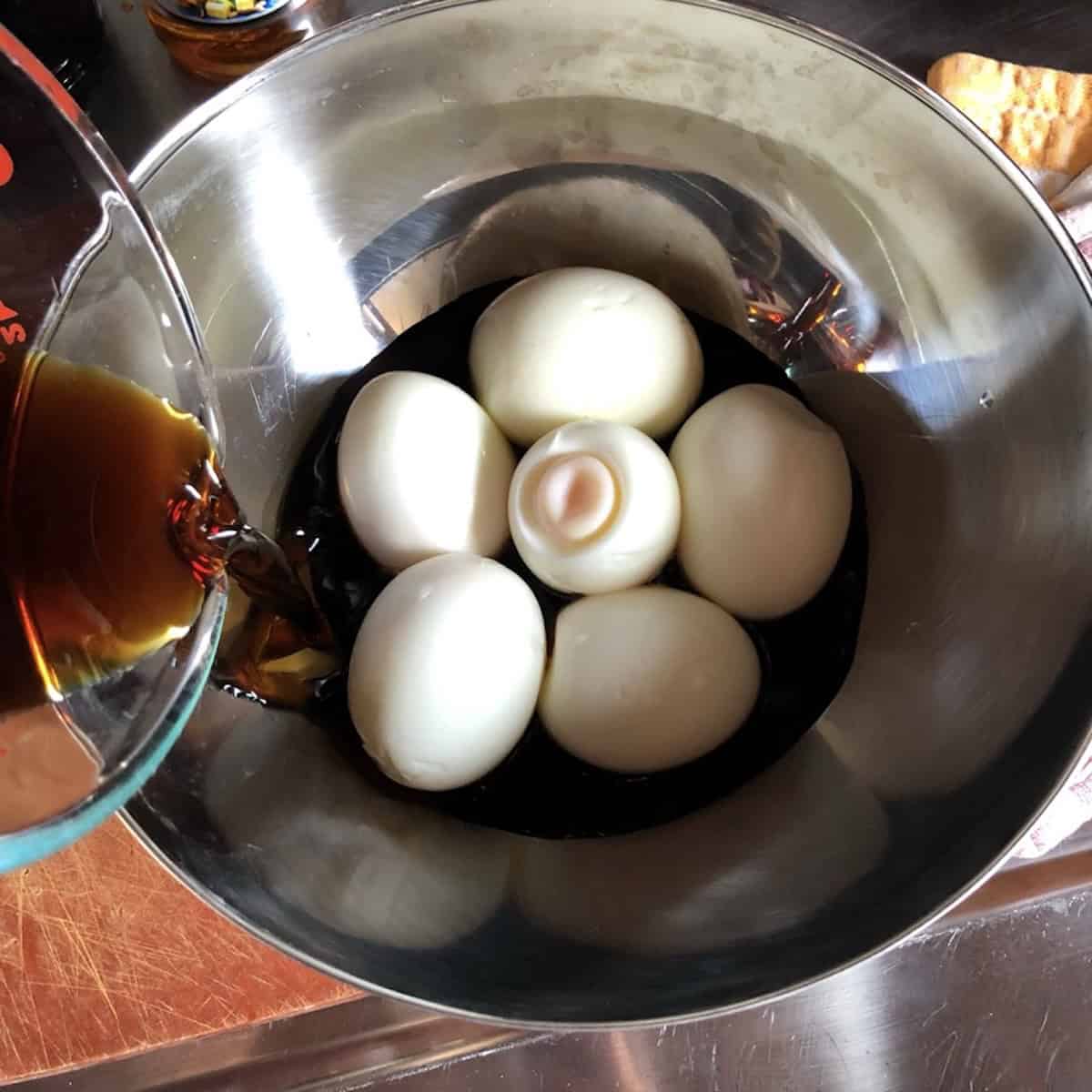 Pouring homemade ramen marinade over soft boiled perfecty cooked ramen eggs in a bowl.
