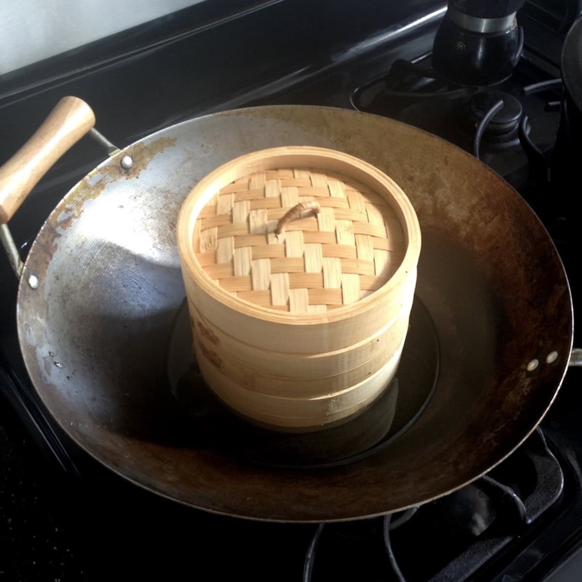 Japanese eggs steaming in a tightly sealed bamboo steamer set inside a wok filled with water to make ramen eggs - alternative soft boiled egg cooking method.