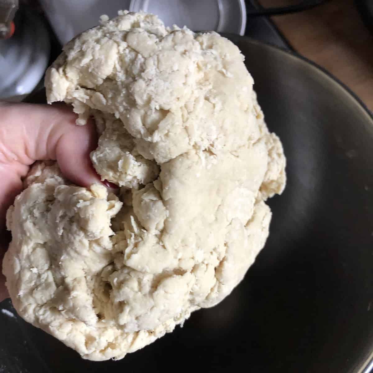 Perfect ramen dough ball held in hand showing cohesive texture after adding remaining alkaline water to bread flour and baked baking soda mixture for homemade ramen noodles recipe how to make ramen dough with proper consistency not tacky or crumbly.
