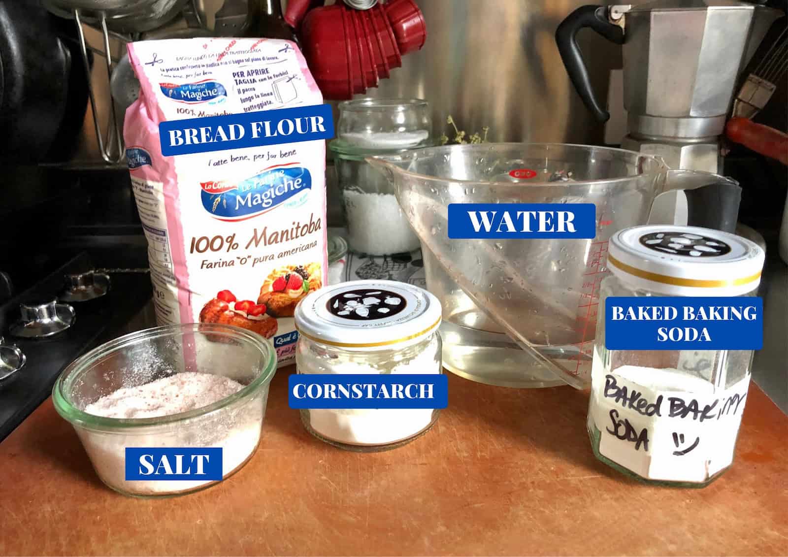 Ramen ingredients labeled on cutting board including bread flour, baked baking soda, water and salt for homemade ramen noodles recipe showing how to make ramen from scratch with alkaline noodle ingredients.
