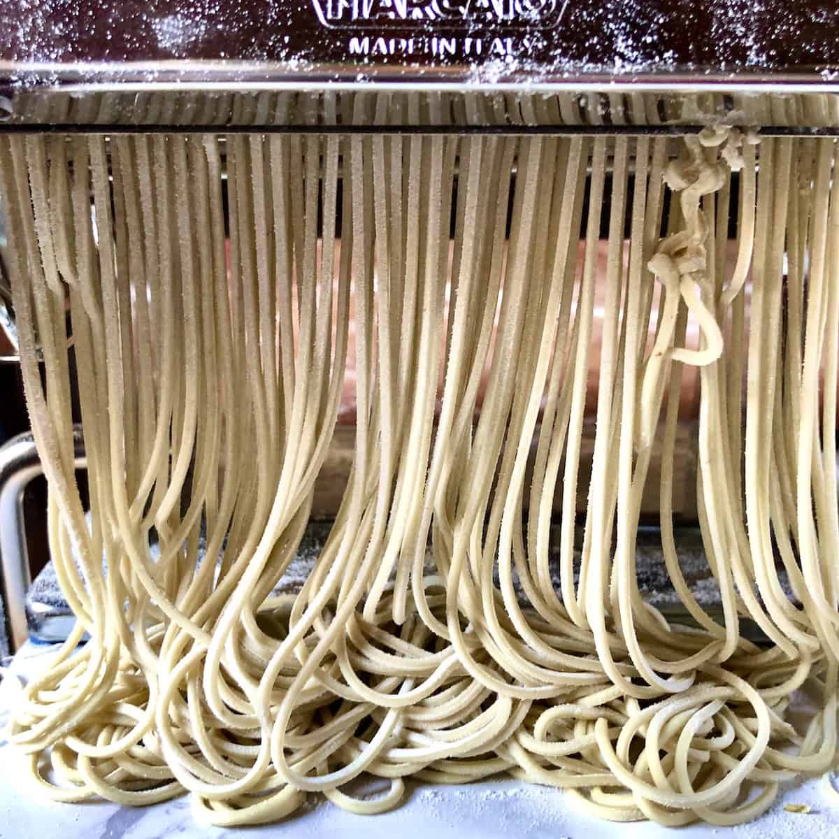 Ramen noodles being cut and coming out of pasta machine homemade ramen noodles recipe alkaline dough cut into thin noodles.