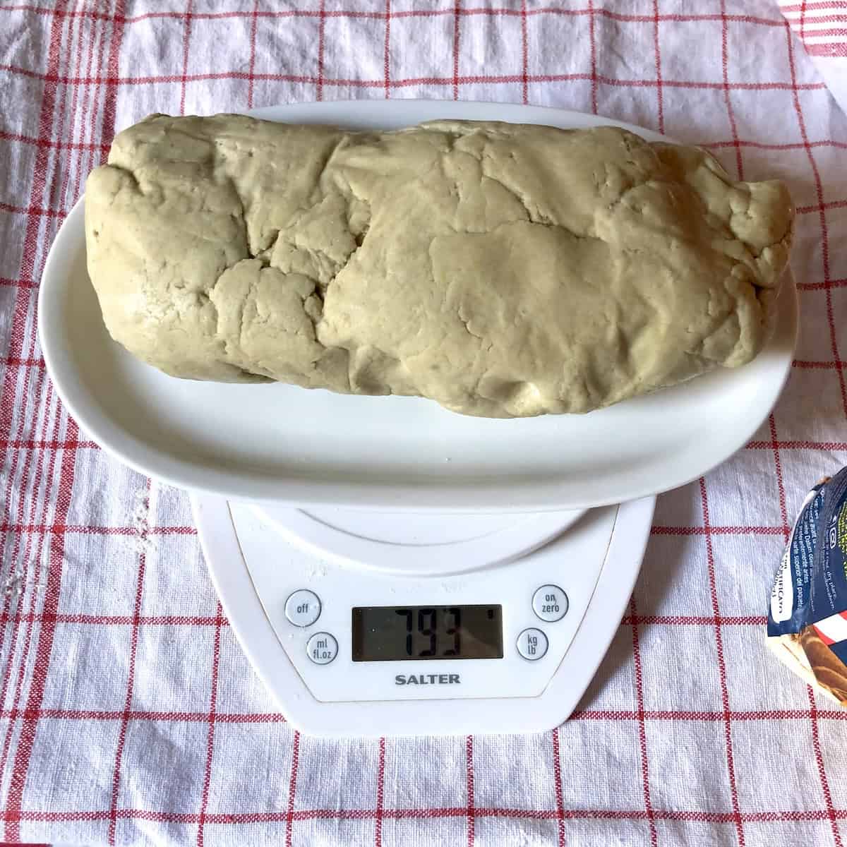 Rested ramen dough on scale being weighed before cutting into four pieces for pasta machine rolling homemade ramen noodles recipe alkaline dough after overnight refrigerator rest how to make ramen preparation step dividing dough.
