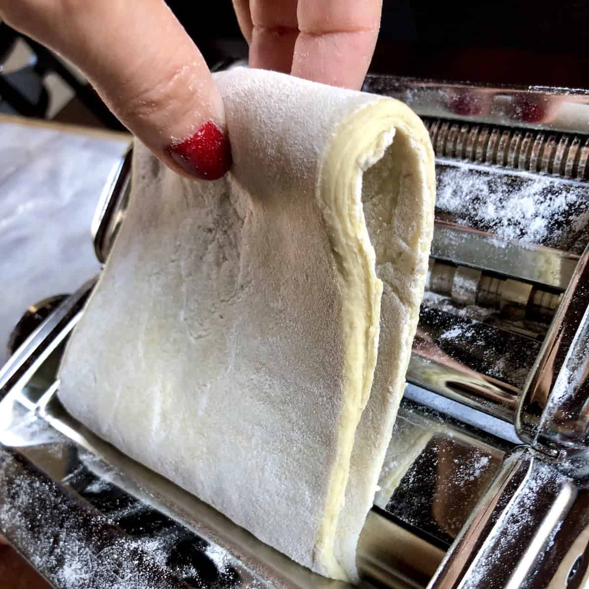 Easy homemade ramen dough being rolled through the pasta machine after being folded in half to create best texture.
