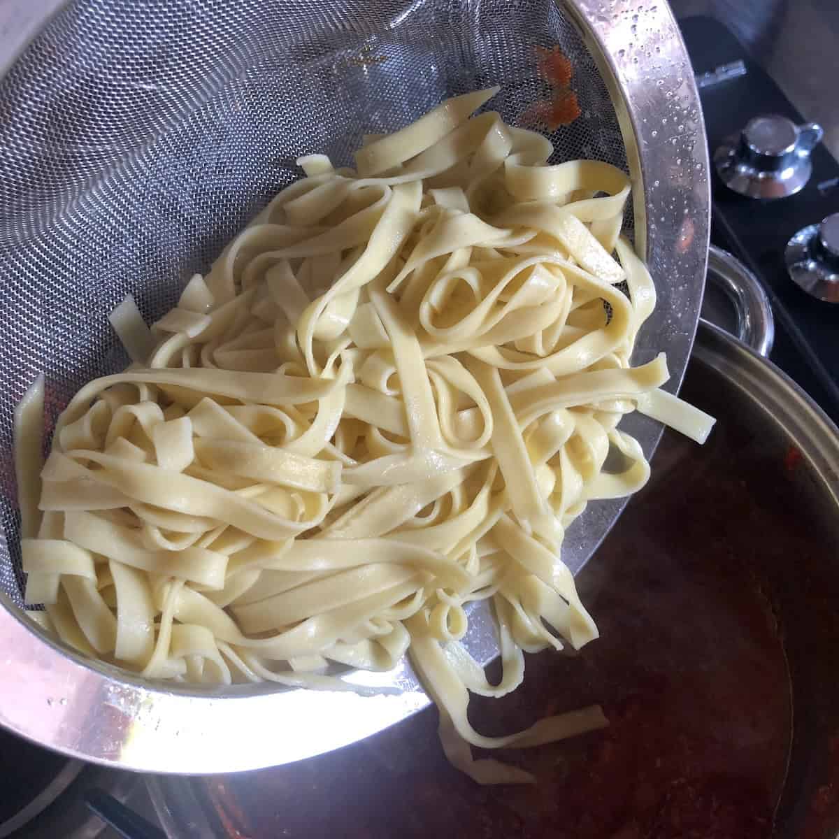 Straining cooked homemade egg noodles in colander after boiling, how to cook egg noodles recipe.
