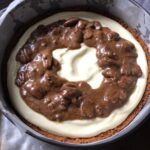cheesecake base poured into prepared springform pan with cookie crust with pecan tassie filling poured in a ring around the outside leaving an open space in the middle