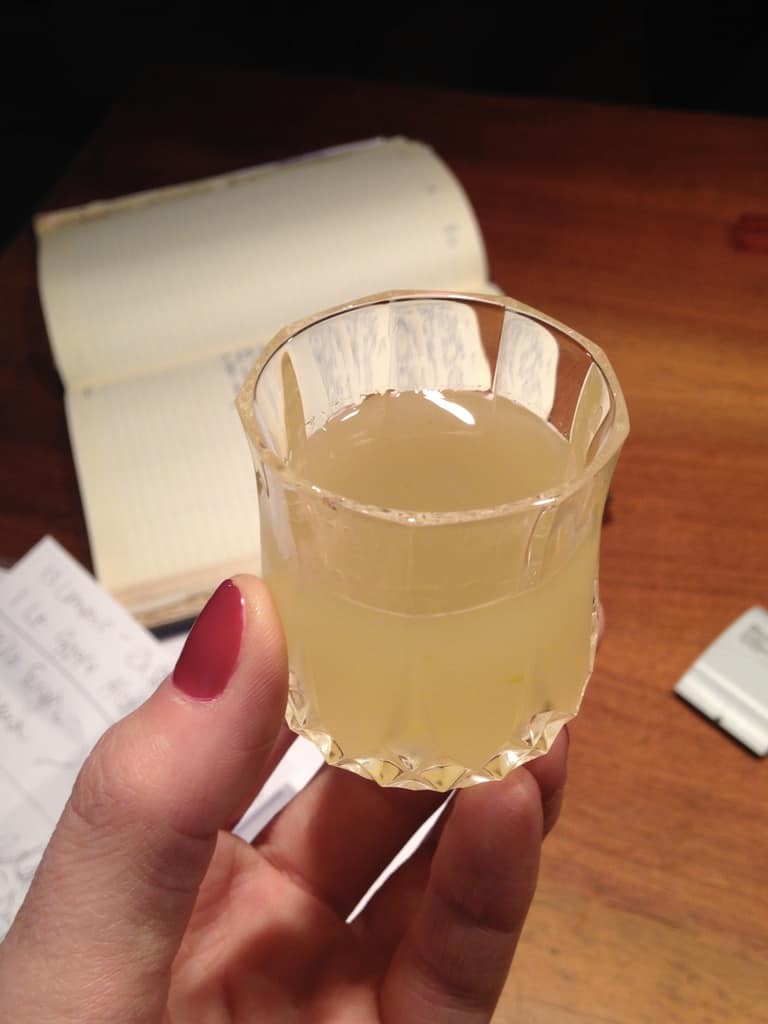 Franco's homemade Limoncello in a small glass I'm holding with the recipes in the background on the table