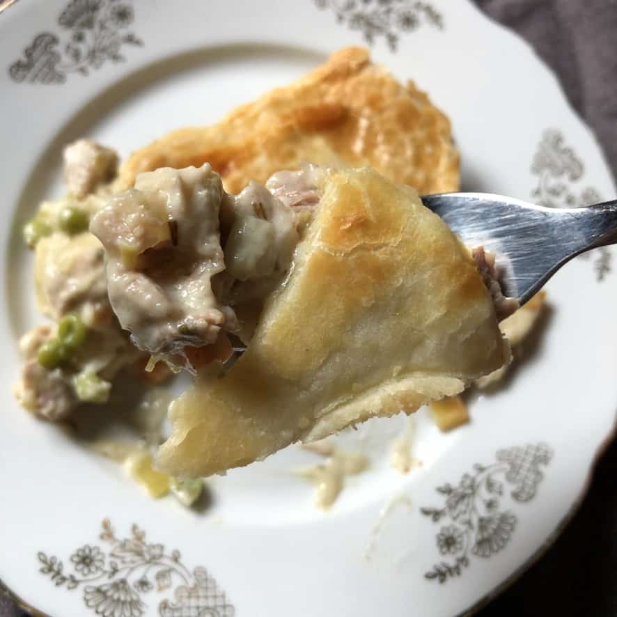 a bite of turkey pot pie with cubed dark and white meat, carrots and peas and a piece of flaky crust