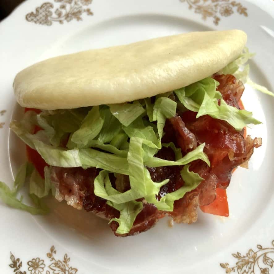 Japanese BLT pork bun on a plate with crispy prosciutto, lettuce, tomato, and sesame-soy spicy mayo