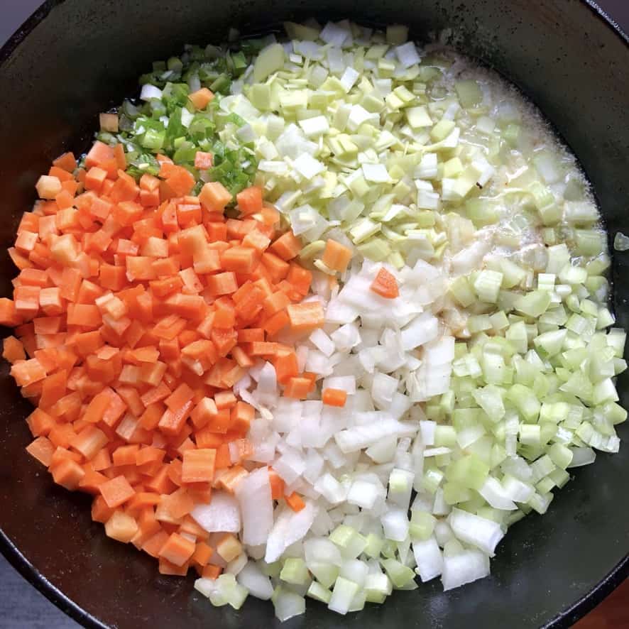 Chopped carrots, onions, leeks, scallions, celery, butter, and poultry seasoning in a cast iron skillet