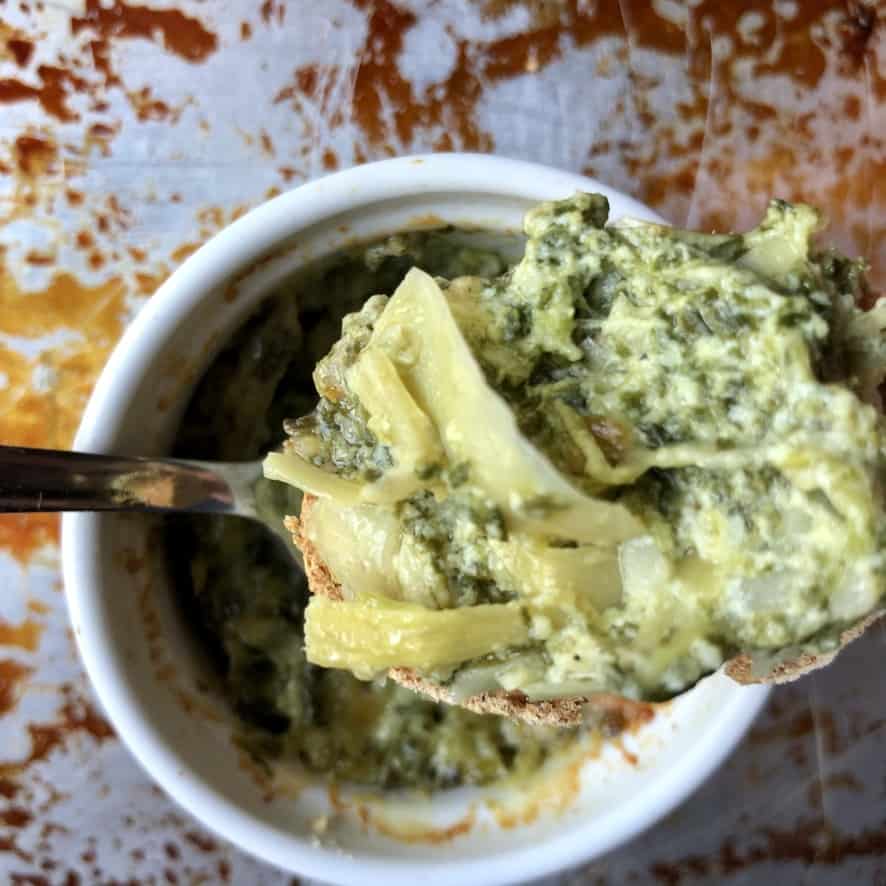 a spoonful of hot dip revealing the whole artichoke leaves