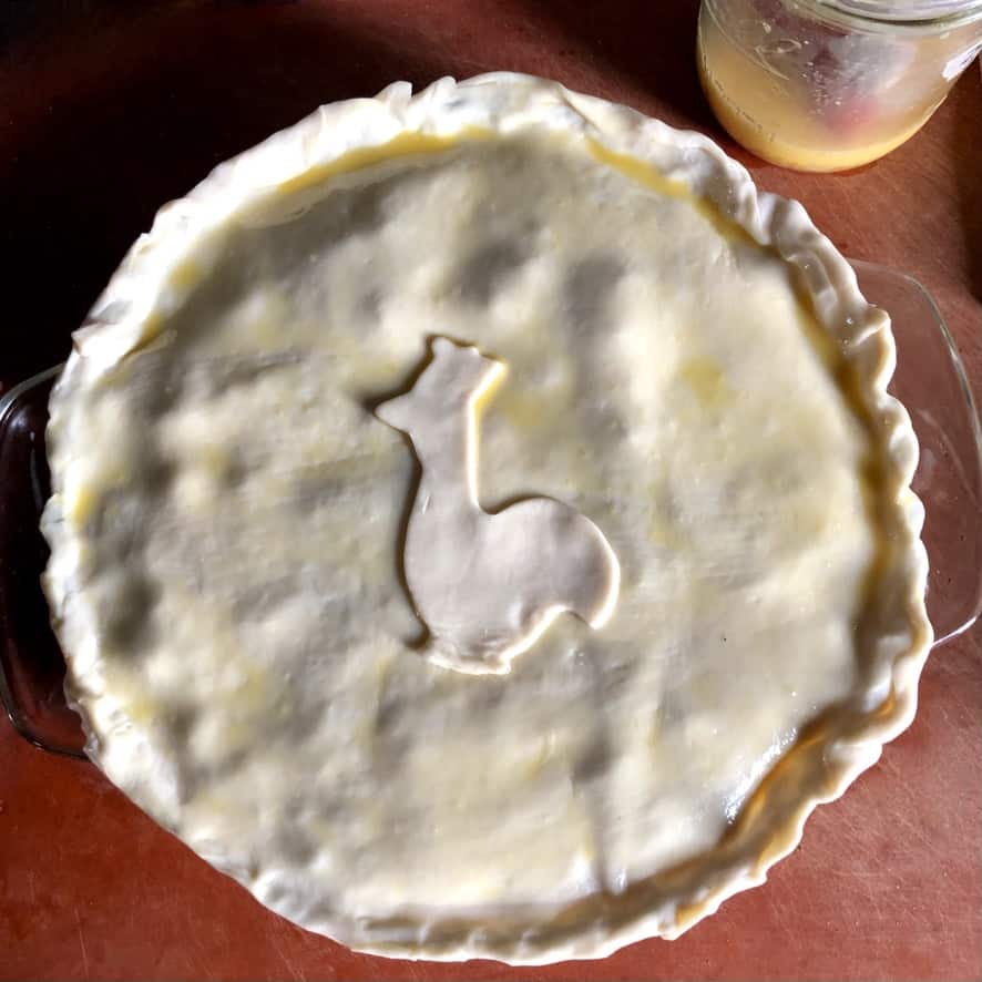 An assembled turkey pot pie with a cutout of a chicken made from extra dough added to the middle and an egg wash brushed over the top