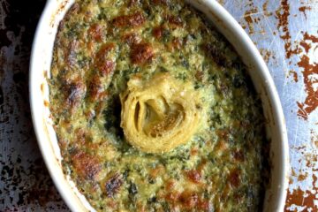 shallow oval ramekin dish with hot golden brown bubbly spinach artichoke dip with a single artichoke heart in the middle.