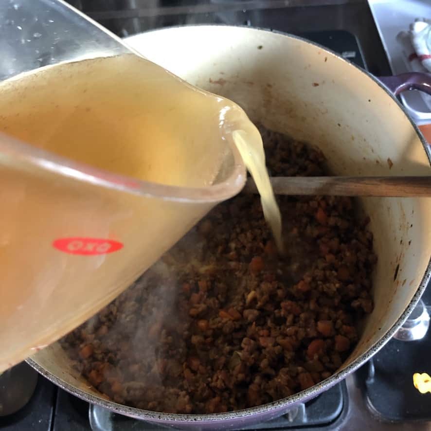 pouring beef stock into the pan with the tomatoes and paste