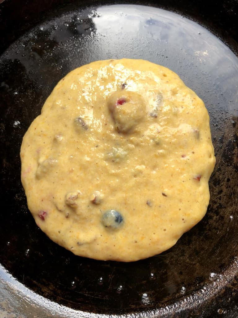 just poured pumpkin pancake batter with red and blue berries and toasted pecans cooking on a crêpe pan
