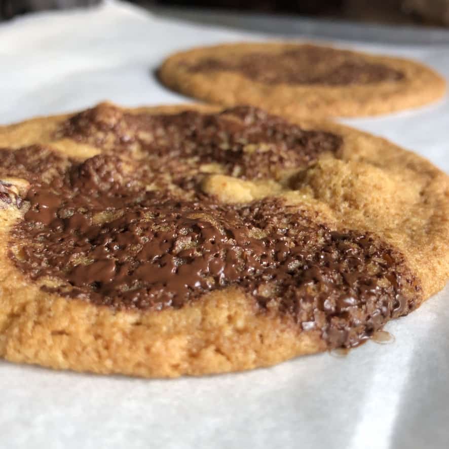 sideview baked chocolate chip pecan cookie very thin, soft, and chewy with large spread
