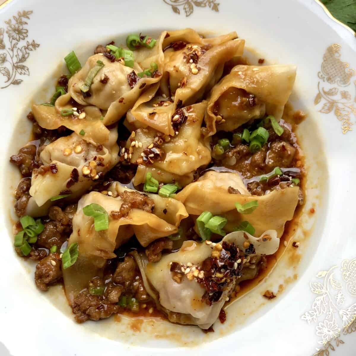 Homemade Sichuan wontons with spicy homemade chili sauce, crispy pork, and scallions in a bowl