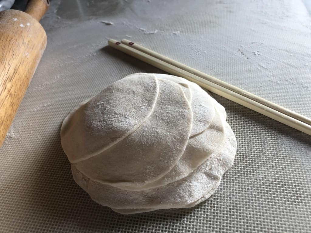 a stack of dumpling wrappers with chopsticks in the background