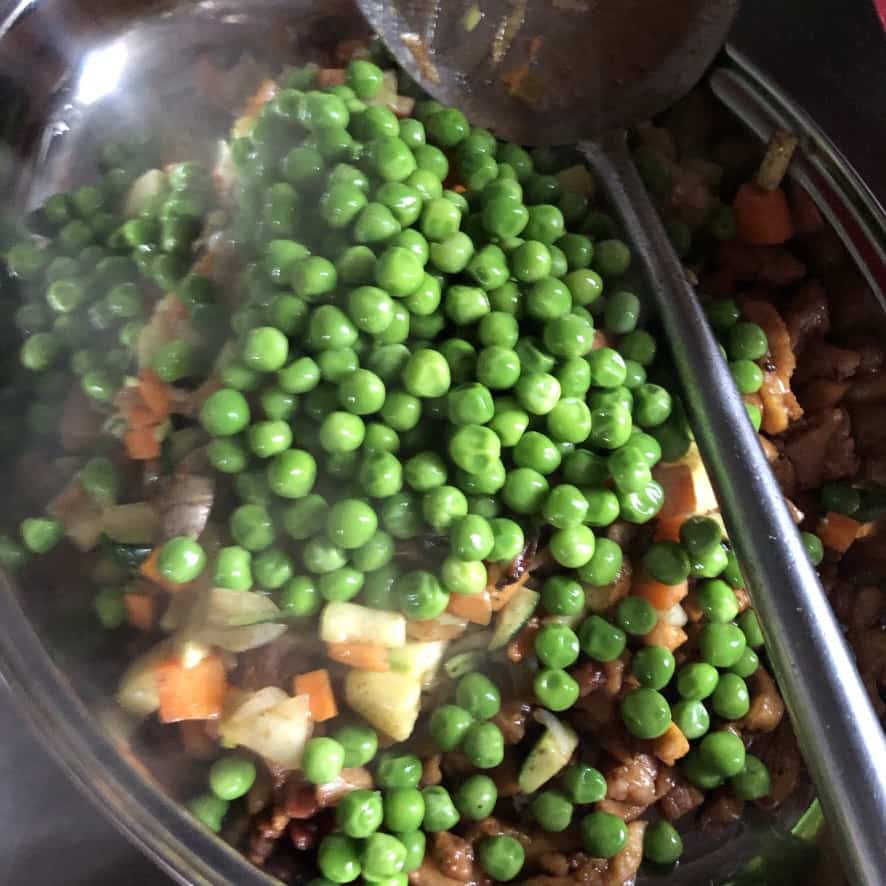 diced carrots, zucchini, mushrooms, onions, scallions, ginger and garlic removed from the wok to a platter and topped with frozen semi-thawed peas