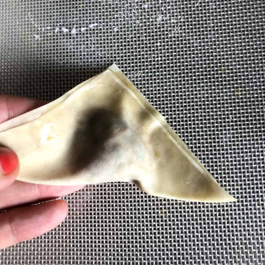 a filled wonton sealed into a triangle shape with all the air removed and the seal close to the filling