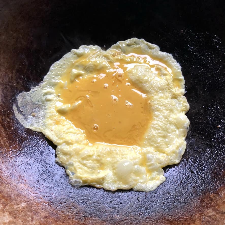 whisked eggs added to a wok and cooked on the outside with a pool of raw egg in the middle