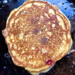 golden brown pumpkin pancake with red and blue berries and toasted pecans cooking on a crêpe pan