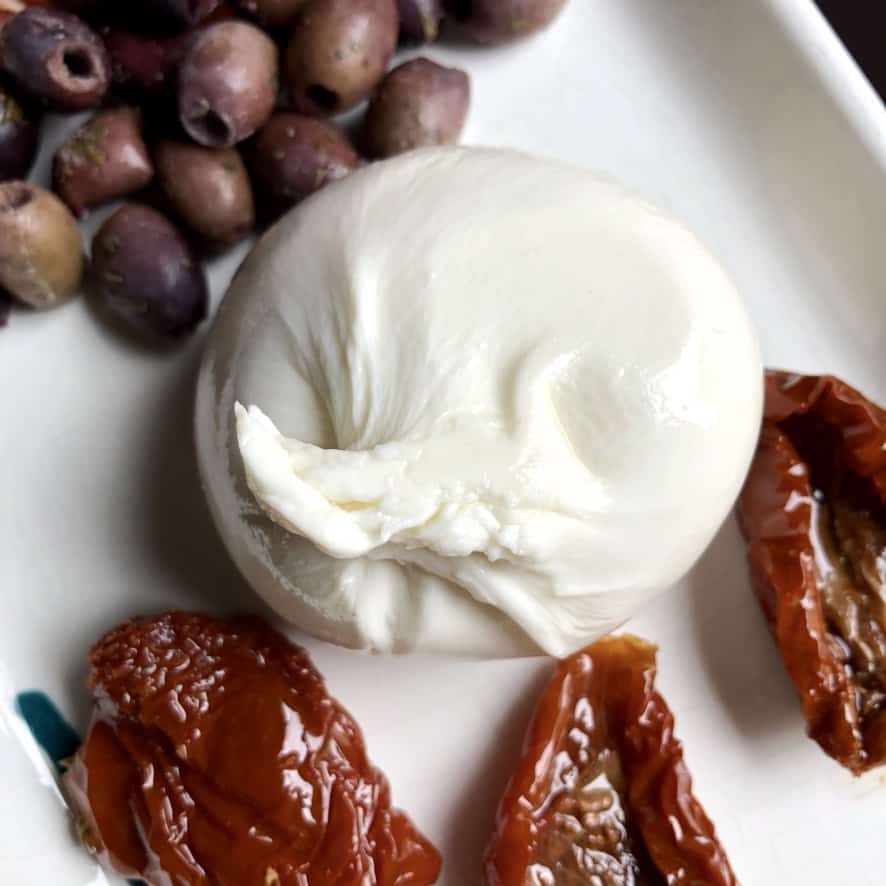 a ball of burrata on a platter with sun dried tomato halves and black olives