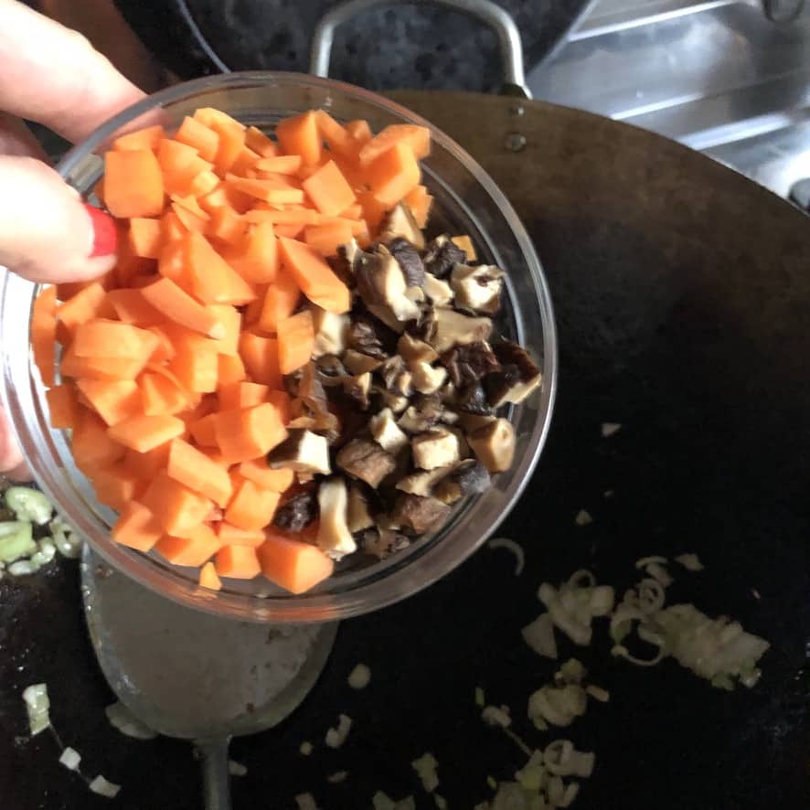 adding the carrots and mushrooms to the wok