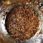 homemade Sichuan Chili oil with one more 1/3 of the oil added with toasted sesame seeds floating on top in a large stainless steel bowl